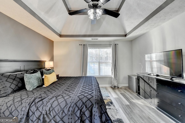 bedroom featuring a raised ceiling, ceiling fan, light hardwood / wood-style floors, and a textured ceiling