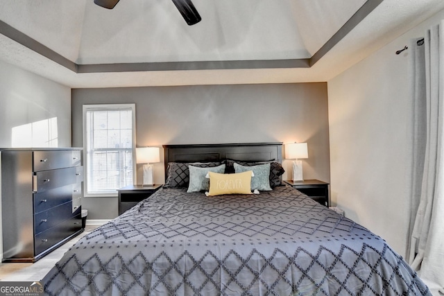 bedroom with ceiling fan, a raised ceiling, and light wood-type flooring