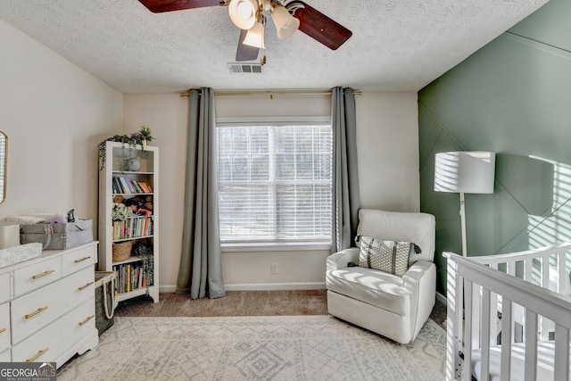 carpeted bedroom featuring a crib, ceiling fan, and a textured ceiling