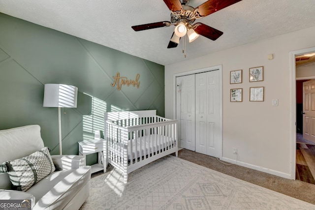 carpeted bedroom featuring a textured ceiling, ceiling fan, a closet, and a crib