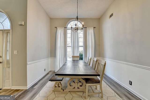 dining space with a textured ceiling, a notable chandelier, and light wood-type flooring