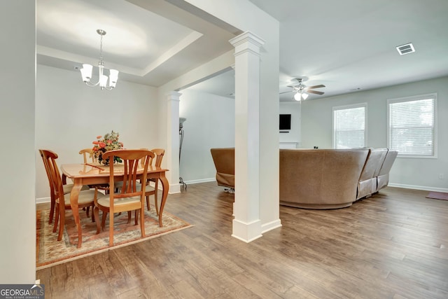 dining area with decorative columns, a raised ceiling, ceiling fan with notable chandelier, and hardwood / wood-style flooring