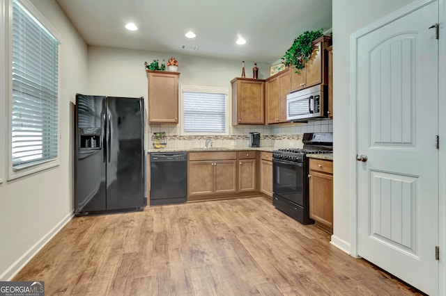 kitchen with decorative backsplash, light stone countertops, light wood-type flooring, sink, and black appliances