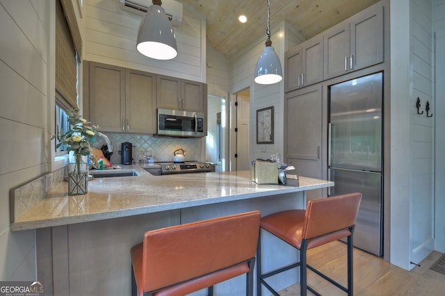 kitchen featuring light hardwood / wood-style flooring, kitchen peninsula, decorative light fixtures, vaulted ceiling, and appliances with stainless steel finishes