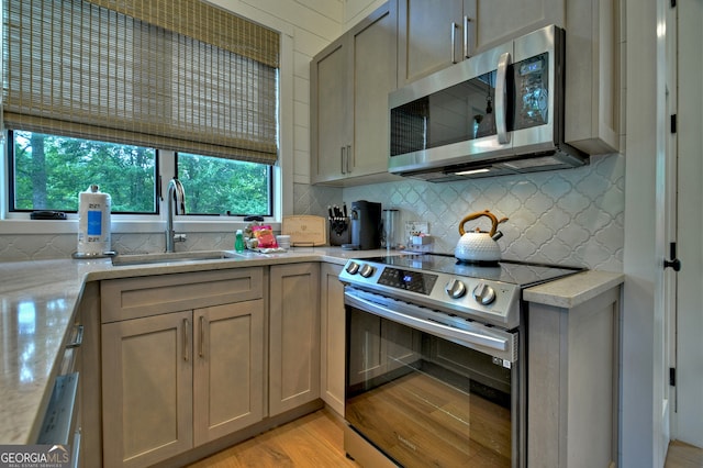 kitchen with light stone countertops, sink, stainless steel appliances, light hardwood / wood-style floors, and decorative backsplash