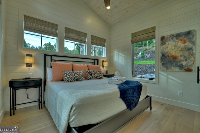 bedroom with wooden walls, light hardwood / wood-style flooring, high vaulted ceiling, and multiple windows