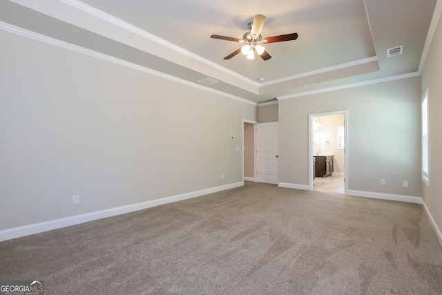 unfurnished bedroom with light carpet, a tray ceiling, ceiling fan, crown molding, and connected bathroom