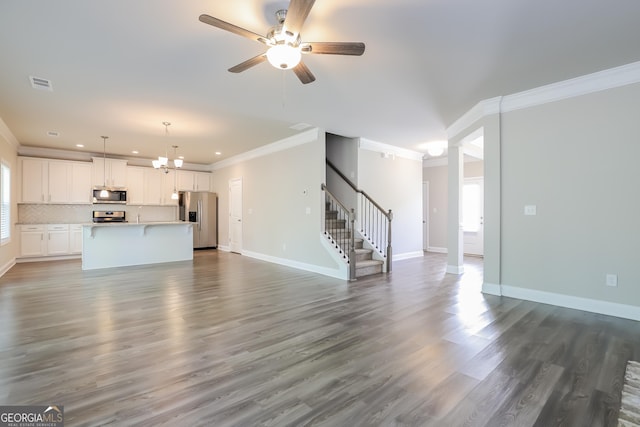 unfurnished living room with ceiling fan with notable chandelier, crown molding, and dark wood-type flooring