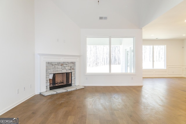 unfurnished living room featuring vaulted ceiling, a fireplace, wood finished floors, baseboards, and visible vents