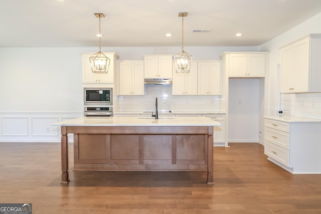 kitchen with light countertops, stainless steel appliances, under cabinet range hood, a sink, and white cabinets