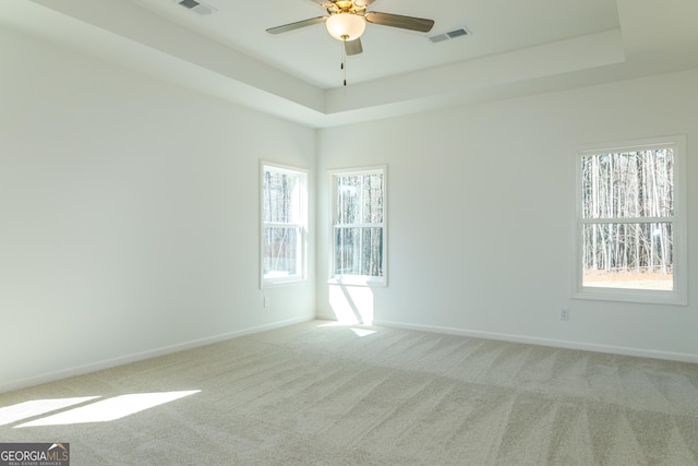 empty room featuring a tray ceiling, baseboards, light colored carpet, visible vents, and ceiling fan