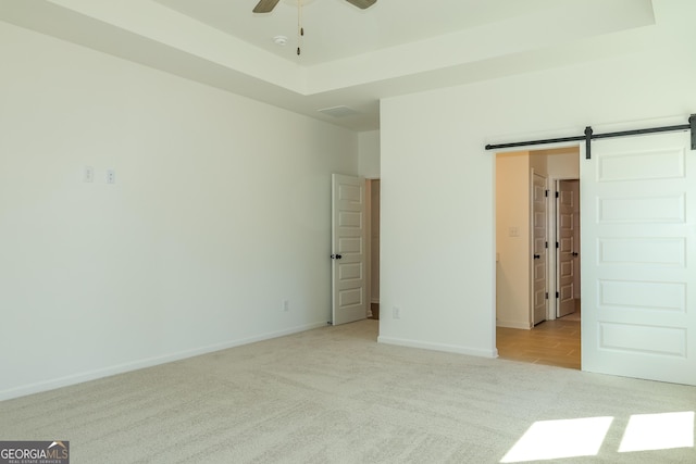empty room with a ceiling fan, light carpet, a raised ceiling, baseboards, and visible vents