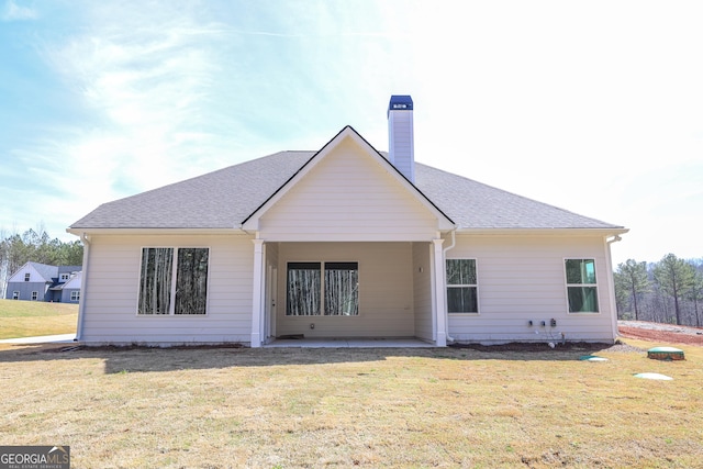 rear view of house with a chimney, a shingled roof, and a yard
