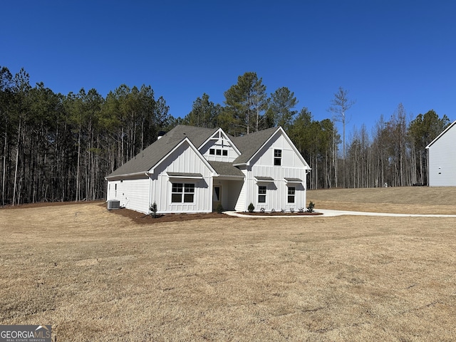 modern inspired farmhouse featuring central AC unit, board and batten siding, a front yard, and a wooded view