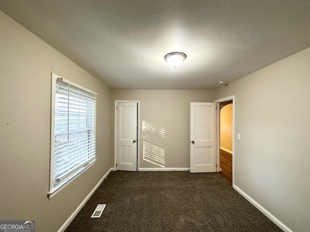 unfurnished bedroom with a textured ceiling and dark colored carpet