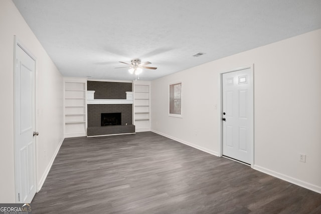 unfurnished living room featuring ceiling fan, dark hardwood / wood-style flooring, a textured ceiling, and a brick fireplace