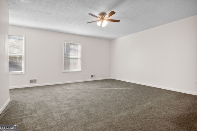 empty room featuring dark colored carpet, ceiling fan, and a textured ceiling