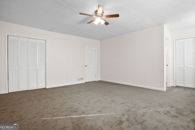 unfurnished bedroom with two closets, dark carpet, and ceiling fan