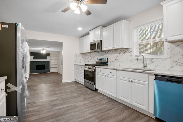 kitchen with appliances with stainless steel finishes, light wood-type flooring, a fireplace, sink, and white cabinets