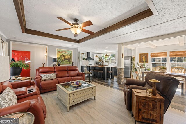 living room featuring ceiling fan, a raised ceiling, light wood-type flooring, and a textured ceiling