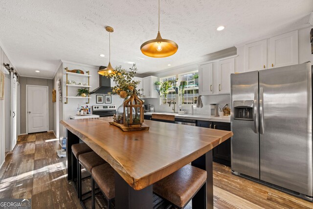 kitchen featuring appliances with stainless steel finishes, wall chimney exhaust hood, pendant lighting, a barn door, and white cabinets