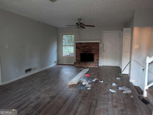 unfurnished living room featuring a textured ceiling, a brick fireplace, ceiling fan, and dark wood-type flooring