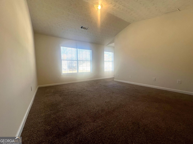 empty room featuring visible vents, dark carpet, a textured ceiling, and baseboards