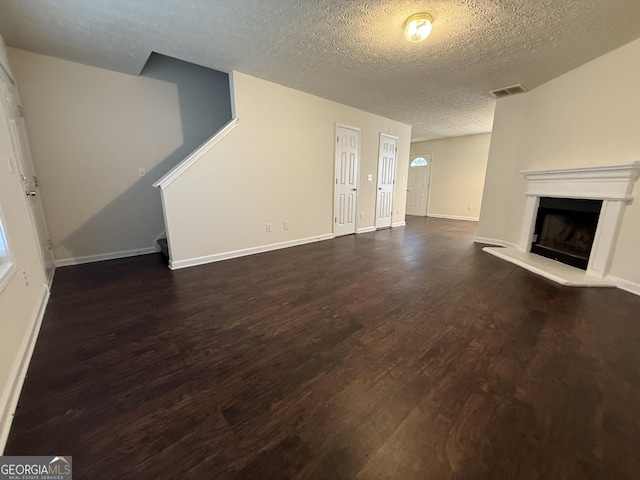 unfurnished living room with a fireplace with raised hearth, a textured ceiling, visible vents, baseboards, and dark wood finished floors