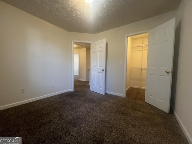 unfurnished bedroom with baseboards, dark carpet, a walk in closet, and a textured ceiling