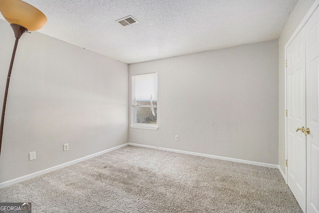 spare room featuring a textured ceiling, carpet floors, visible vents, and baseboards