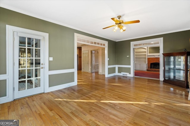 unfurnished living room featuring hardwood / wood-style floors, a brick fireplace, ceiling fan, and crown molding