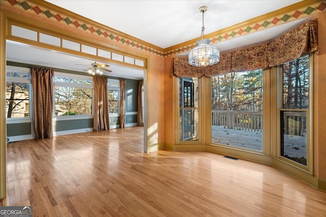 unfurnished dining area with ceiling fan with notable chandelier, light hardwood / wood-style floors, and crown molding