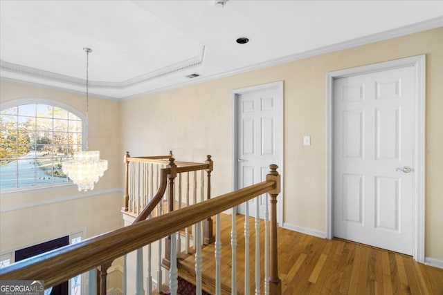 corridor with a raised ceiling, hardwood / wood-style flooring, crown molding, and a notable chandelier