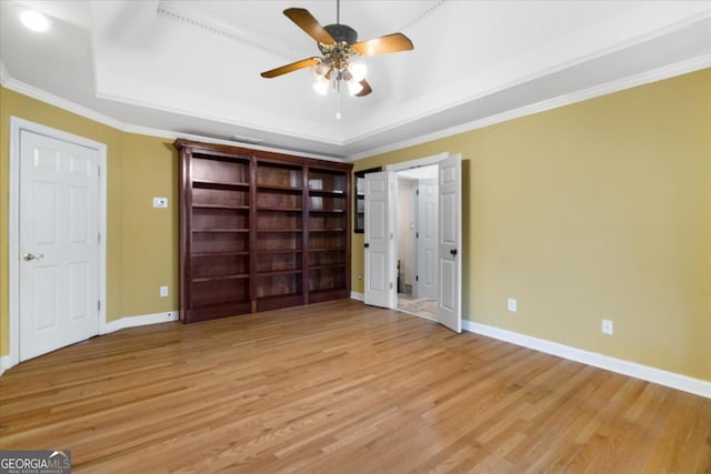 unfurnished bedroom featuring light wood-type flooring, a tray ceiling, and crown molding