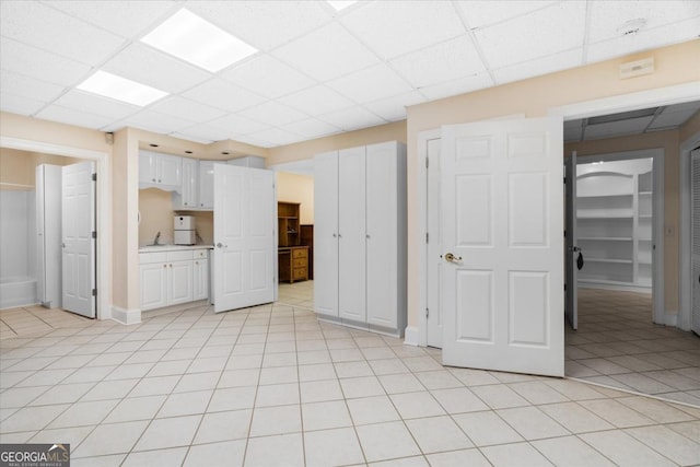 interior space with a paneled ceiling, white cabinetry, and light tile patterned floors