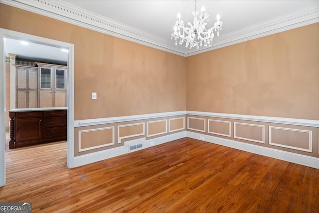 spare room featuring light wood-type flooring, an inviting chandelier, and crown molding