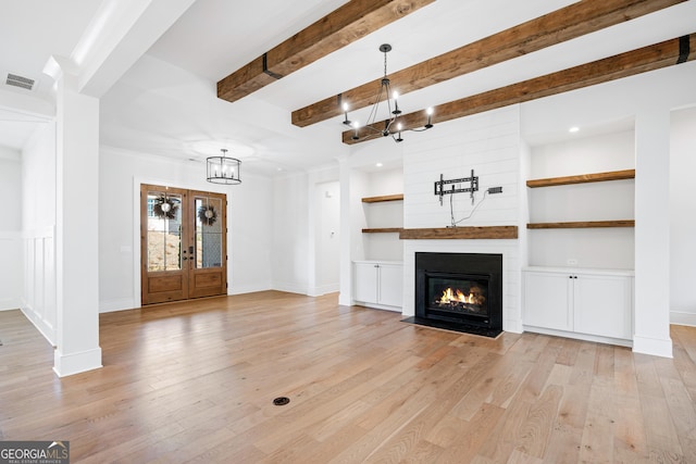 unfurnished living room with an inviting chandelier, french doors, crown molding, light hardwood / wood-style flooring, and a large fireplace