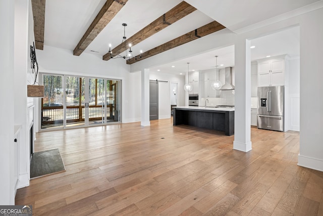 unfurnished living room with beam ceiling, a barn door, sink, and light hardwood / wood-style flooring