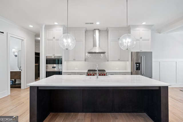 kitchen with high end refrigerator, double wall oven, wall chimney exhaust hood, light stone countertops, and an island with sink