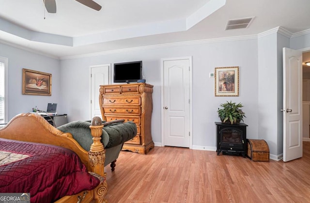 bedroom featuring a tray ceiling, a wood stove, ceiling fan, and light wood-type flooring