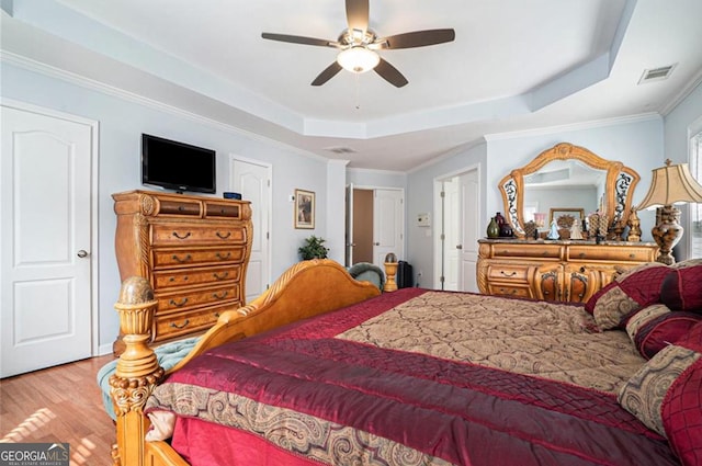 bedroom with hardwood / wood-style flooring, ceiling fan, crown molding, and a tray ceiling