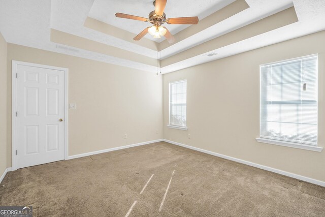 unfurnished room with a raised ceiling, ceiling fan, and carpet flooring