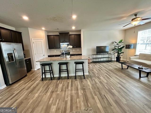 kitchen featuring stainless steel appliances, light stone counters, light hardwood / wood-style flooring, a kitchen bar, and a kitchen island with sink