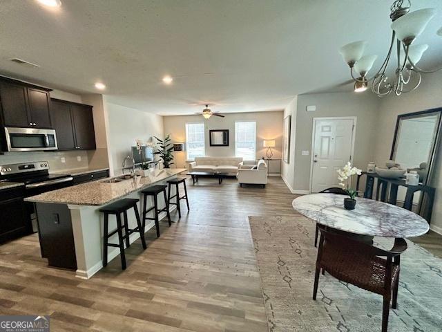 kitchen featuring light stone countertops, stainless steel appliances, sink, wood-type flooring, and an island with sink