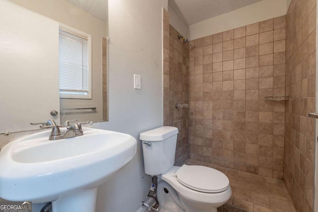 bathroom with tiled shower, toilet, and sink