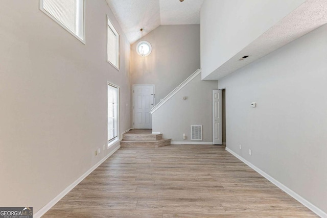 foyer with a textured ceiling, light wood-type flooring, high vaulted ceiling, and plenty of natural light