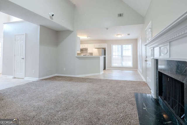 unfurnished living room featuring high vaulted ceiling, light carpet, and a high end fireplace