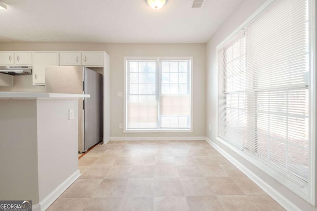 kitchen featuring white cabinets, stainless steel refrigerator, and range hood