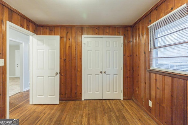 unfurnished bedroom with wood-type flooring, crown molding, a closet, and wooden walls