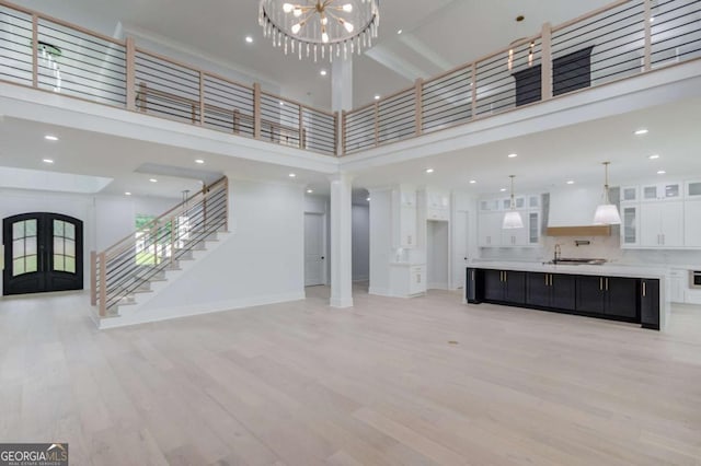 unfurnished living room featuring sink, french doors, a high ceiling, a notable chandelier, and light hardwood / wood-style floors